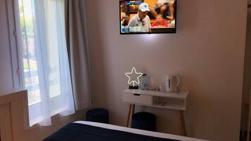 A hotel room with a bed, a desk with a star-shaped light, a television displaying a golf tournament, and a window with curtains.