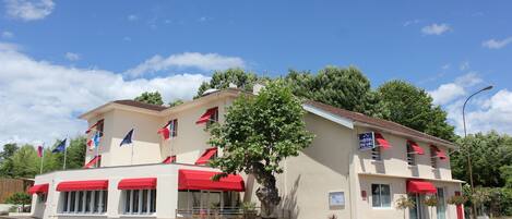 Un hotel con toldo rojo, varias banderas y un árbol en primer plano.