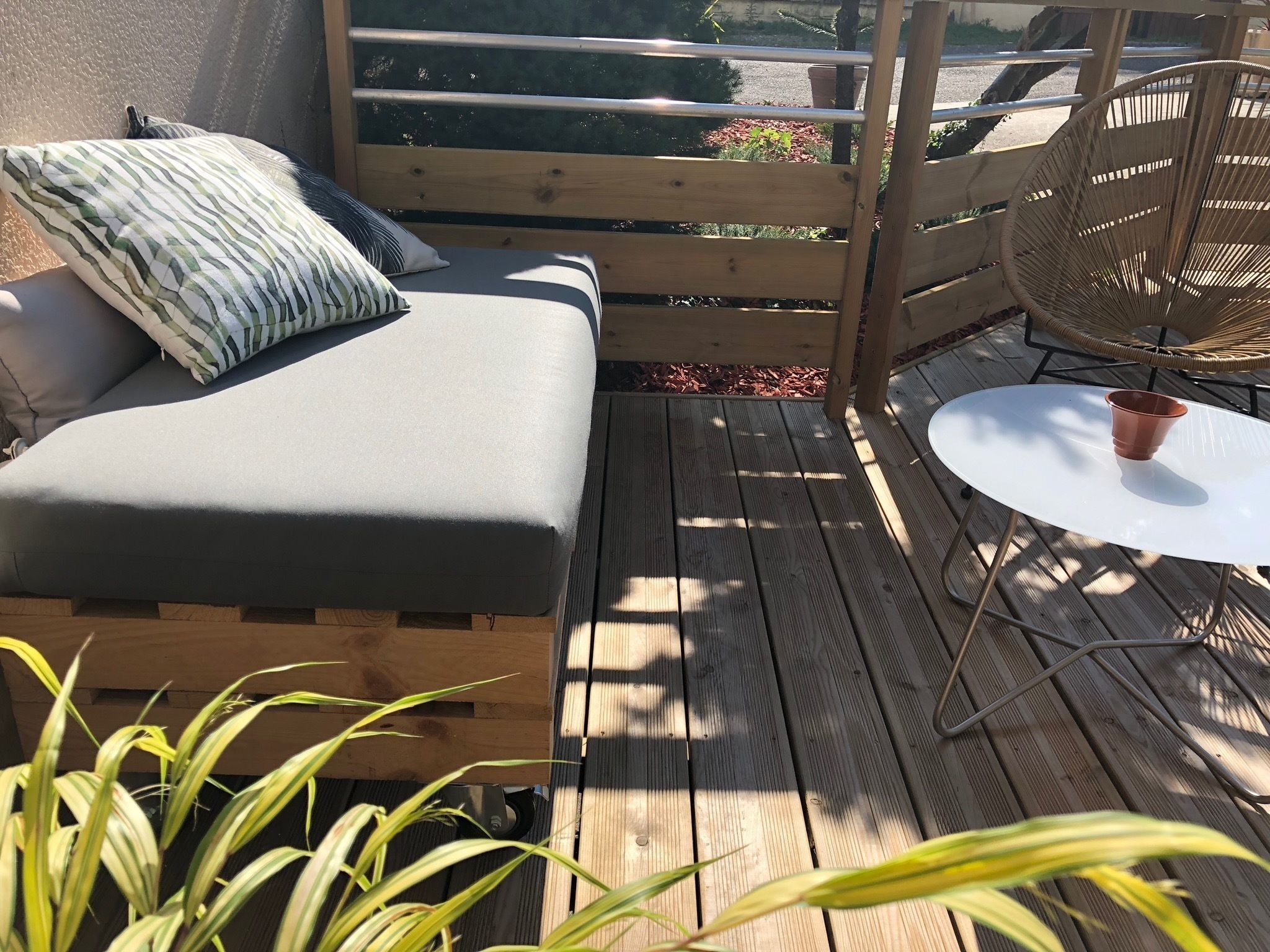 Une terrasse en bois avec un coin salon doté de coussins, une petite table ronde et une chaise en osier.