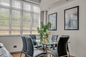 A modern dining area with a glass table, black chairs, and a vase of flowers. - Luxurious Lawrence House Serviced Apartment (London)