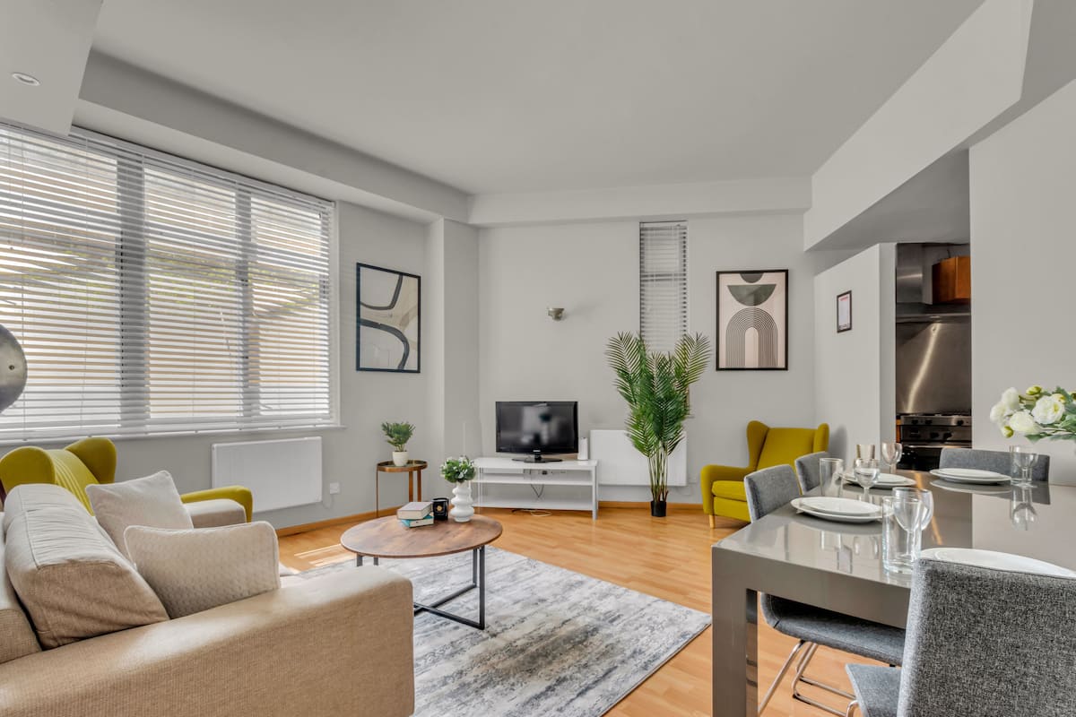 Ein modernes Wohnzimmer mit Sofa, Couchtisch, Fernseher, Esstisch mit Stühlen und Küchenzeile.