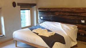 Una cama con cabecera de madera, ventana con vistas y suelo de baldosas.