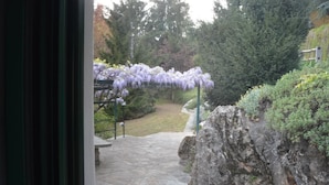 Un sendero de piedra que conduce a un jardín con un arco de glicinas y una formación rocosa.