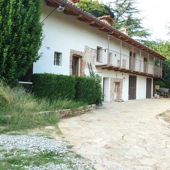 A two-story house with a stone facade, a balcony on the upper floor, and a paved driveway. - L'Uovo e La Faina (Busca)