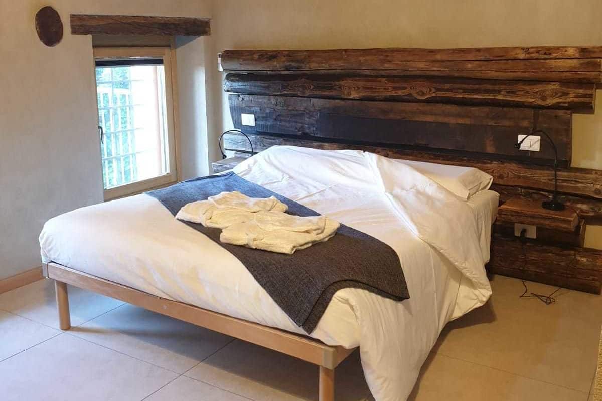 A bedroom with a wooden headboard, a bed with white bedding, a window, and a small table with a lamp.