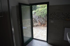 A bathroom with a stone-tiled floor, a glass door leading to a stone wall, and a tiled backsplash. - L'Uovo e La Faina (Busca)