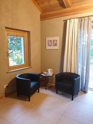 A room with two black armchairs, a small round table with a kettle, a framed map on the wall, and a window with curtains. - L'Uovo e La Faina (Busca)