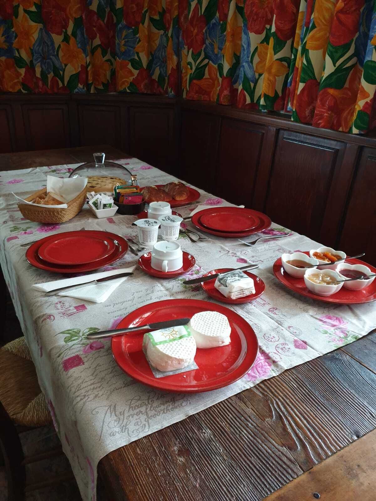 A dining table set with red plates, bowls, and a basket of bread.