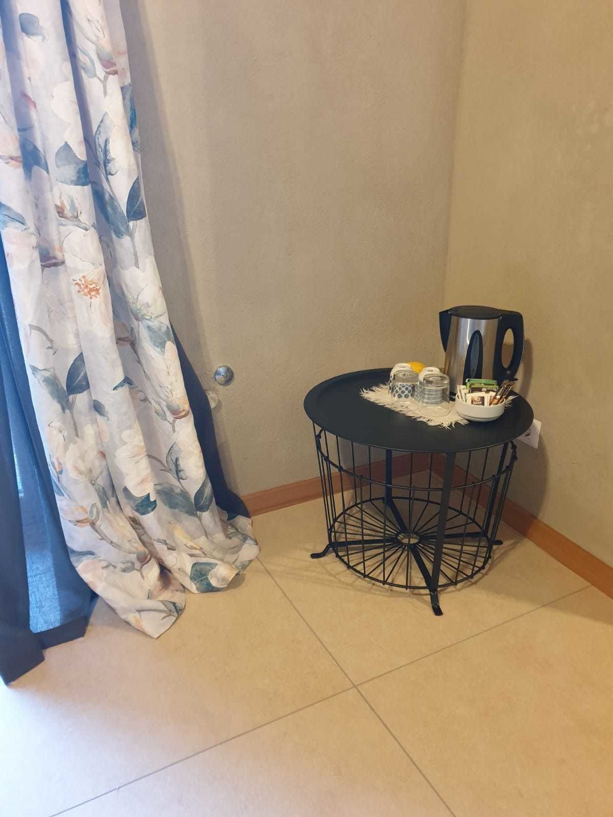 A small room with a round metal table, a coffee maker, and a curtain with a floral pattern.