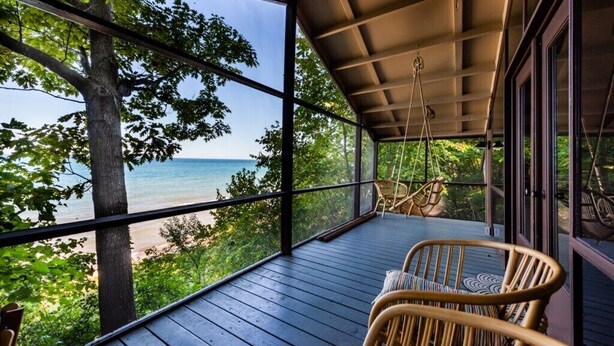 A covered outdoor area with a view of the beach, wooden flooring, and wicker chairs. - HARBERT PRIVATE LAKEFRONT HOME WITH PRIVATE HOT TUB! (Harbert)