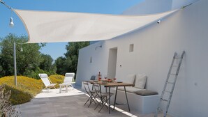 Eine Terrasse im Freien mit Tisch und Stühlen, einer weißen Wand und einem weißen Baldachin.