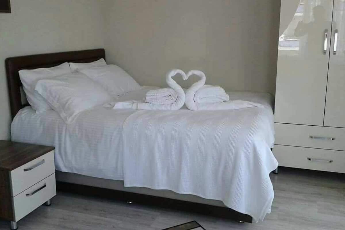 A neatly made bed with white linens and two towels arranged in a heart shape.