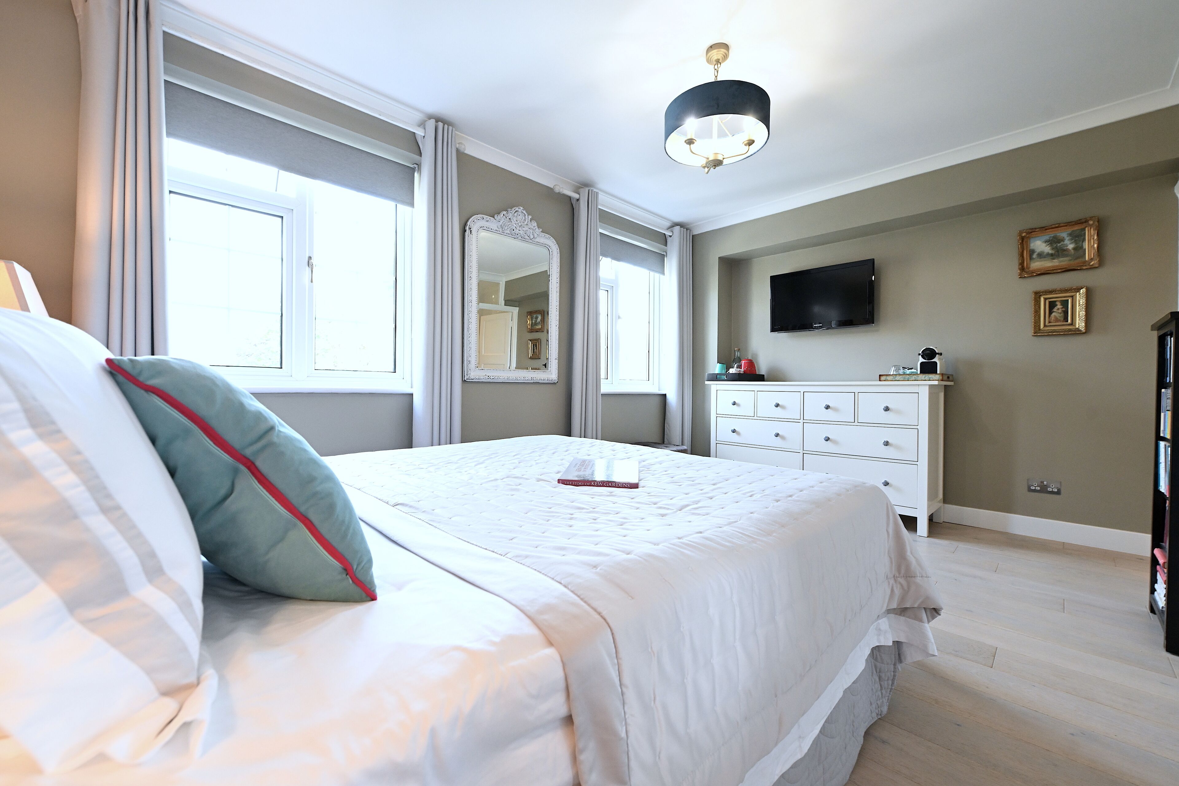 A bedroom with a large bed, a dresser, a television mounted on the wall, and a window with curtains.