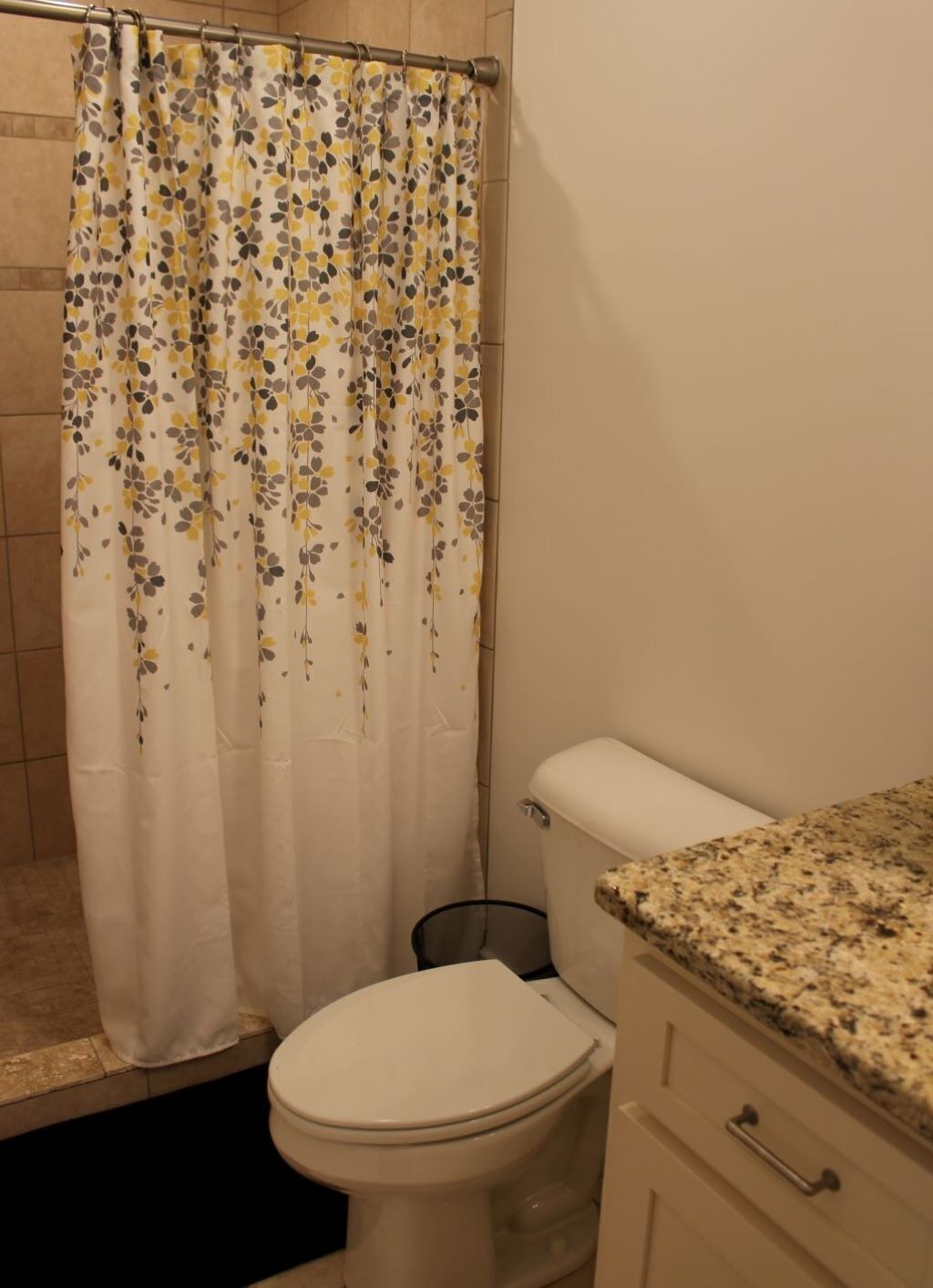 Ein Badezimmer mit Toilette, einem Waschbecken mit Granitablage und einer Duschvorhang mit Blumenmuster.