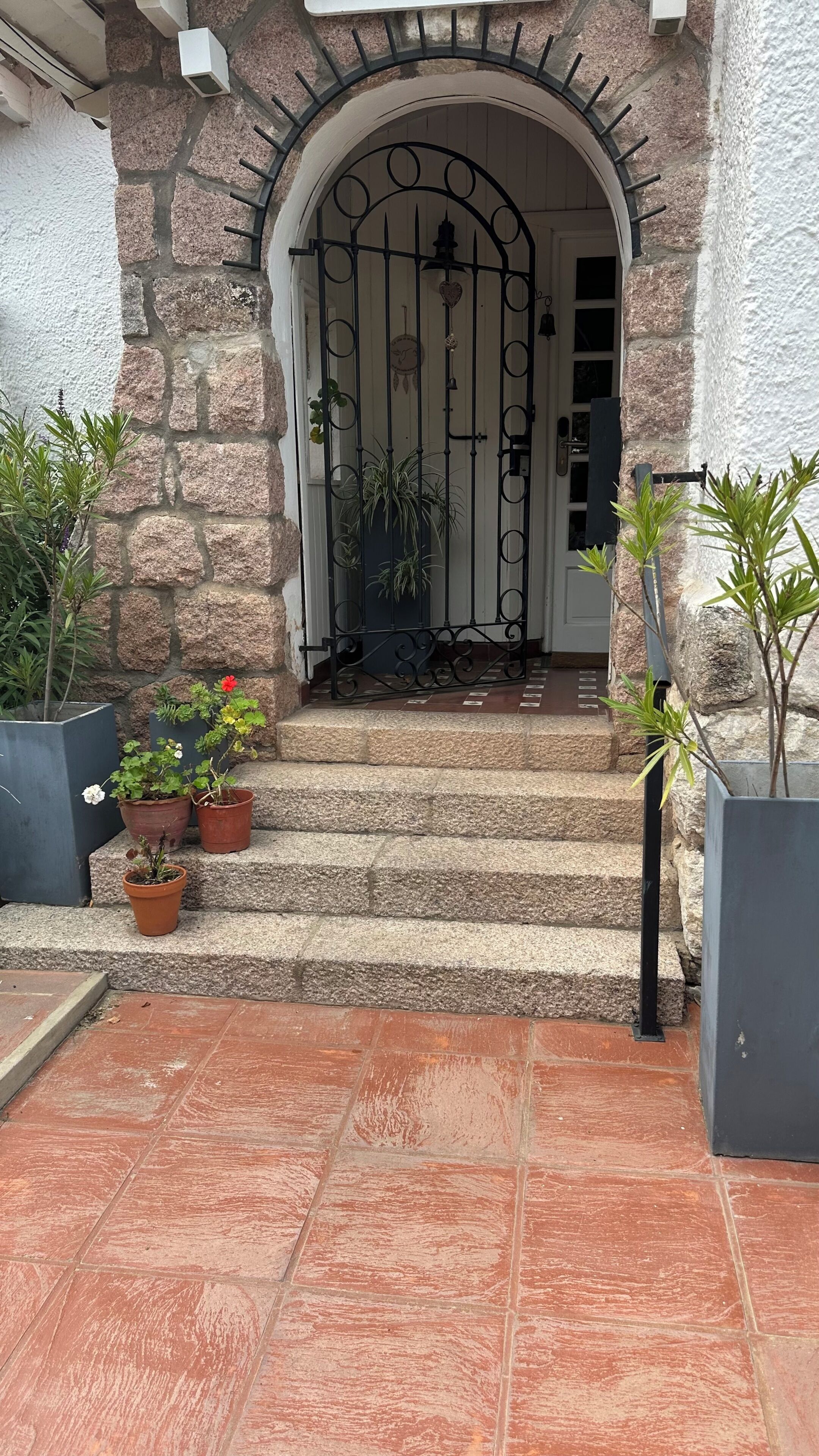 Une entrée en pierre avec un portail en métal, des plantes en pot et un chemin dallé menant à une porte.