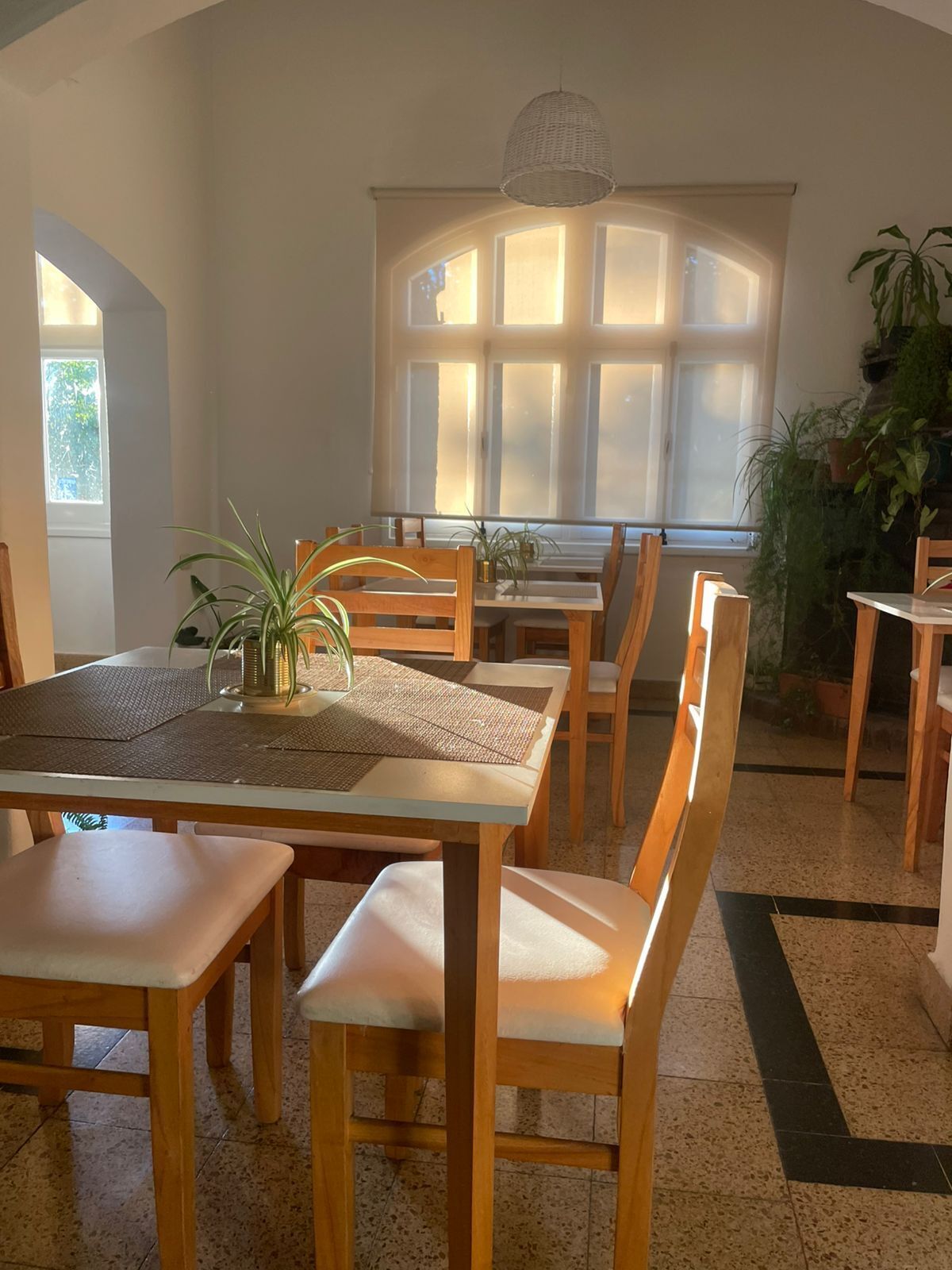 Een eetruimte met een tafel, stoelen en een groot raam met zonlicht.