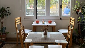 Un comedor con mesa y sillas, ventanas amplias y plantas en macetas.