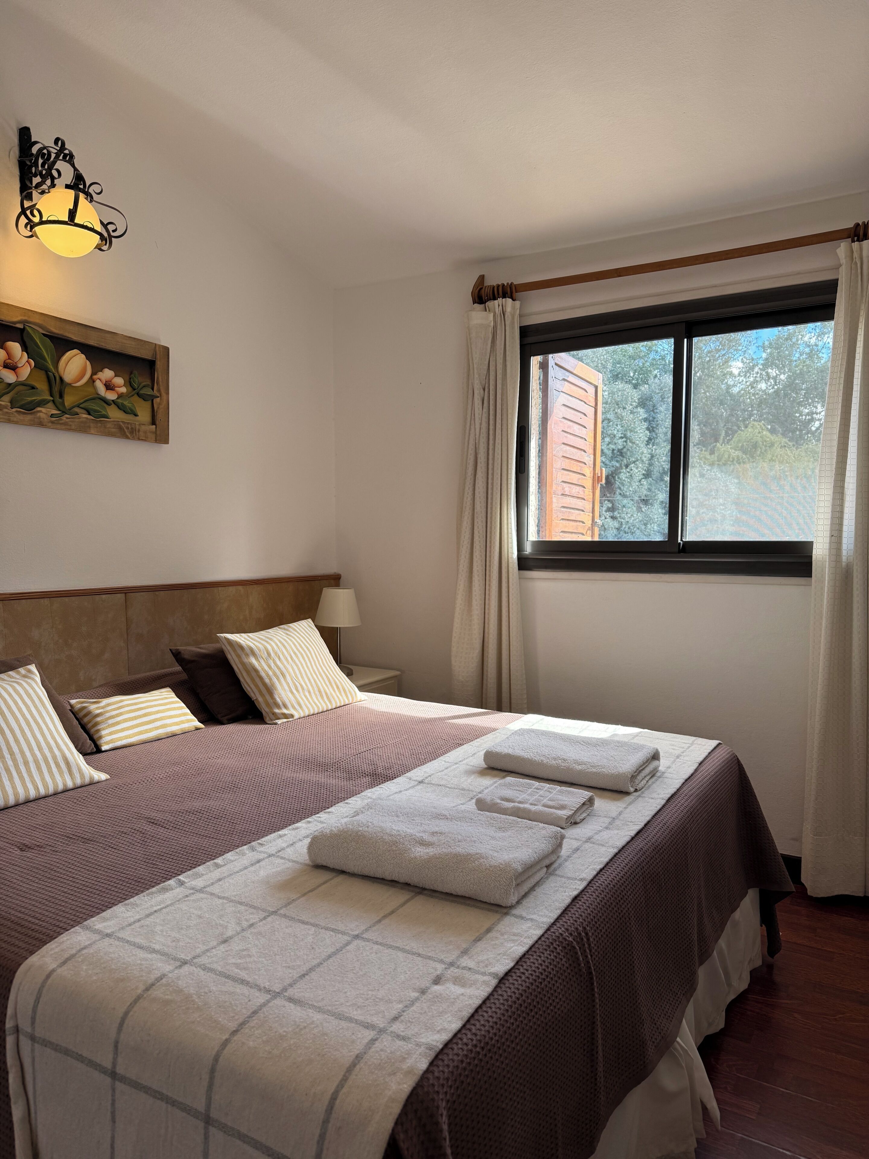 Un lit bien fait, avec une couvre-lit à carreaux, une tête de lit et un tableau de fleurs accroché au mur.