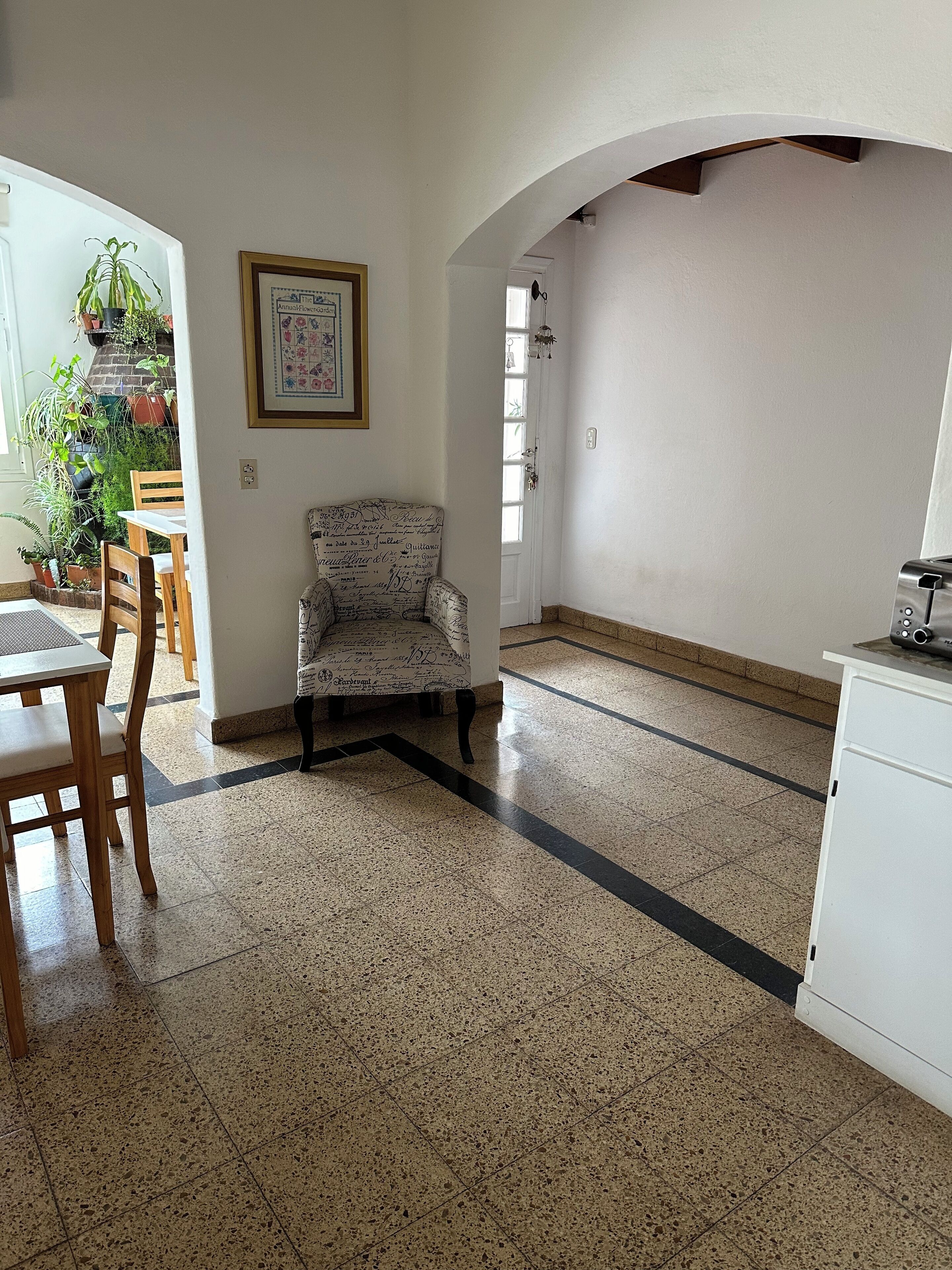 A spacious room with a tiled floor, a wooden dining table, a patterned armchair, and a white cabinet.