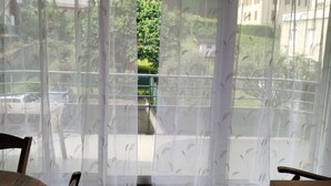 A room with a view of a green landscape through a window with sheer curtains.