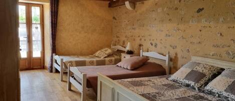 A rustic bedroom with two single beds, wooden beams, a patterned wall, and a door leading outside.