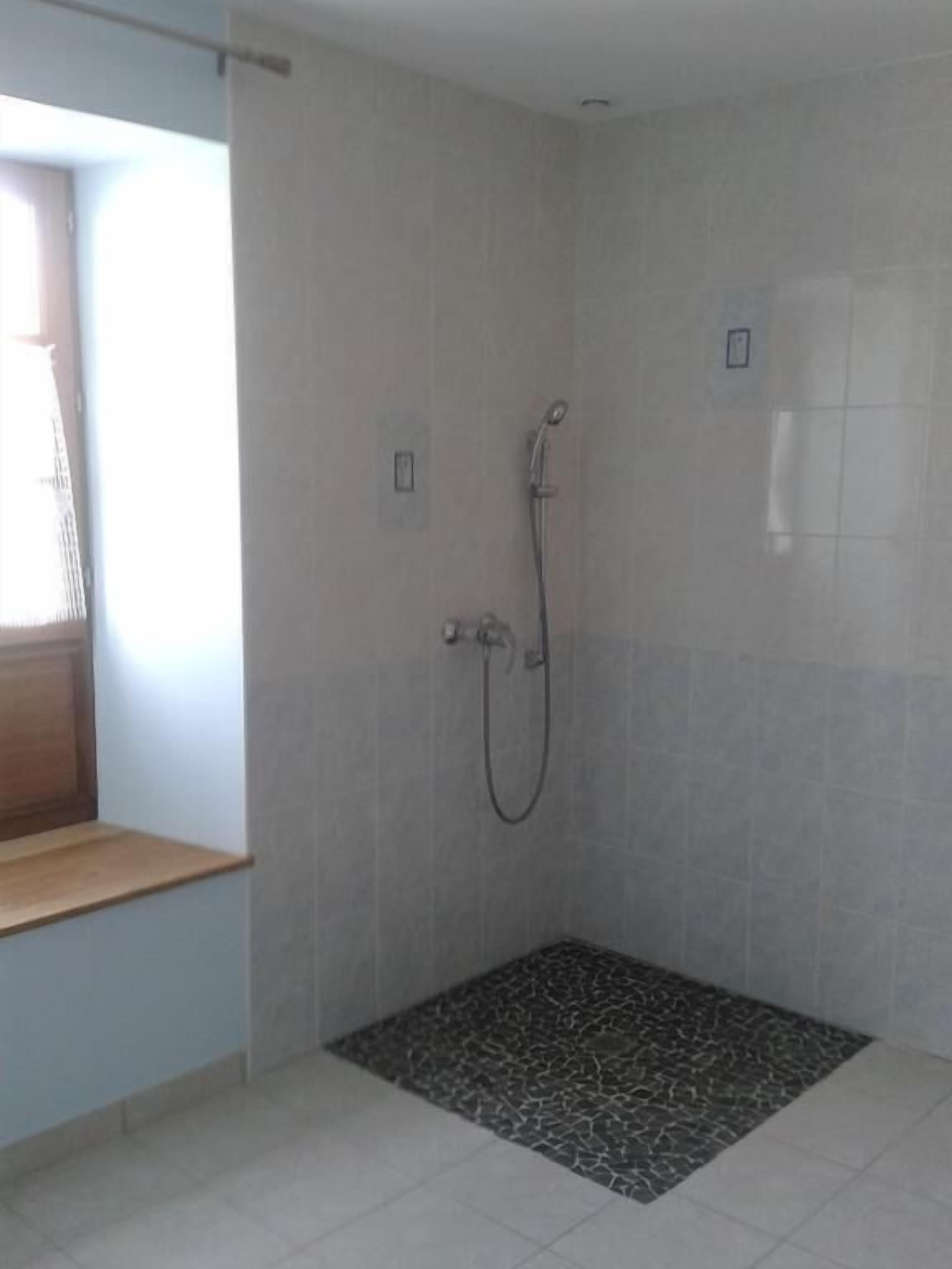 Un petit espace de douche fermé, doté d’un sol carrelé et d’un pommeau de douche.