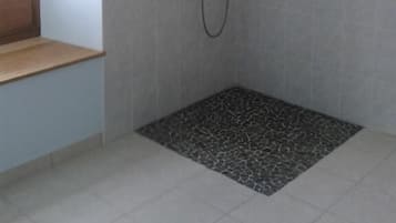 Un petit espace de douche fermé, doté d’un sol carrelé et d’un pommeau de douche.