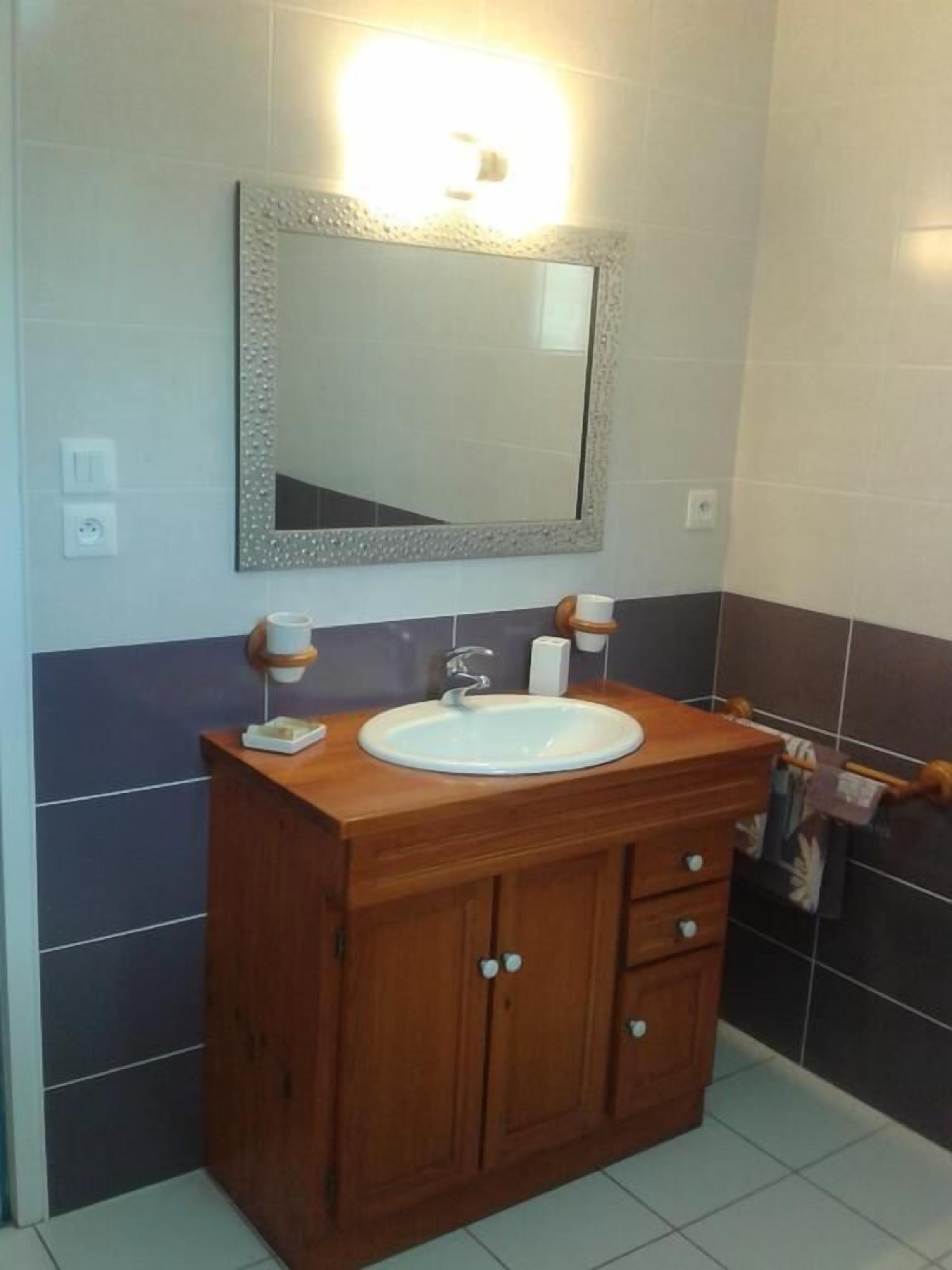 A bathroom with a wooden vanity, a white sink, a mirror with a decorative frame, and a wall-mounted light.
