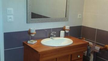 A bathroom with a wooden vanity, a white sink, a mirror with a decorative frame, and a wall-mounted light.