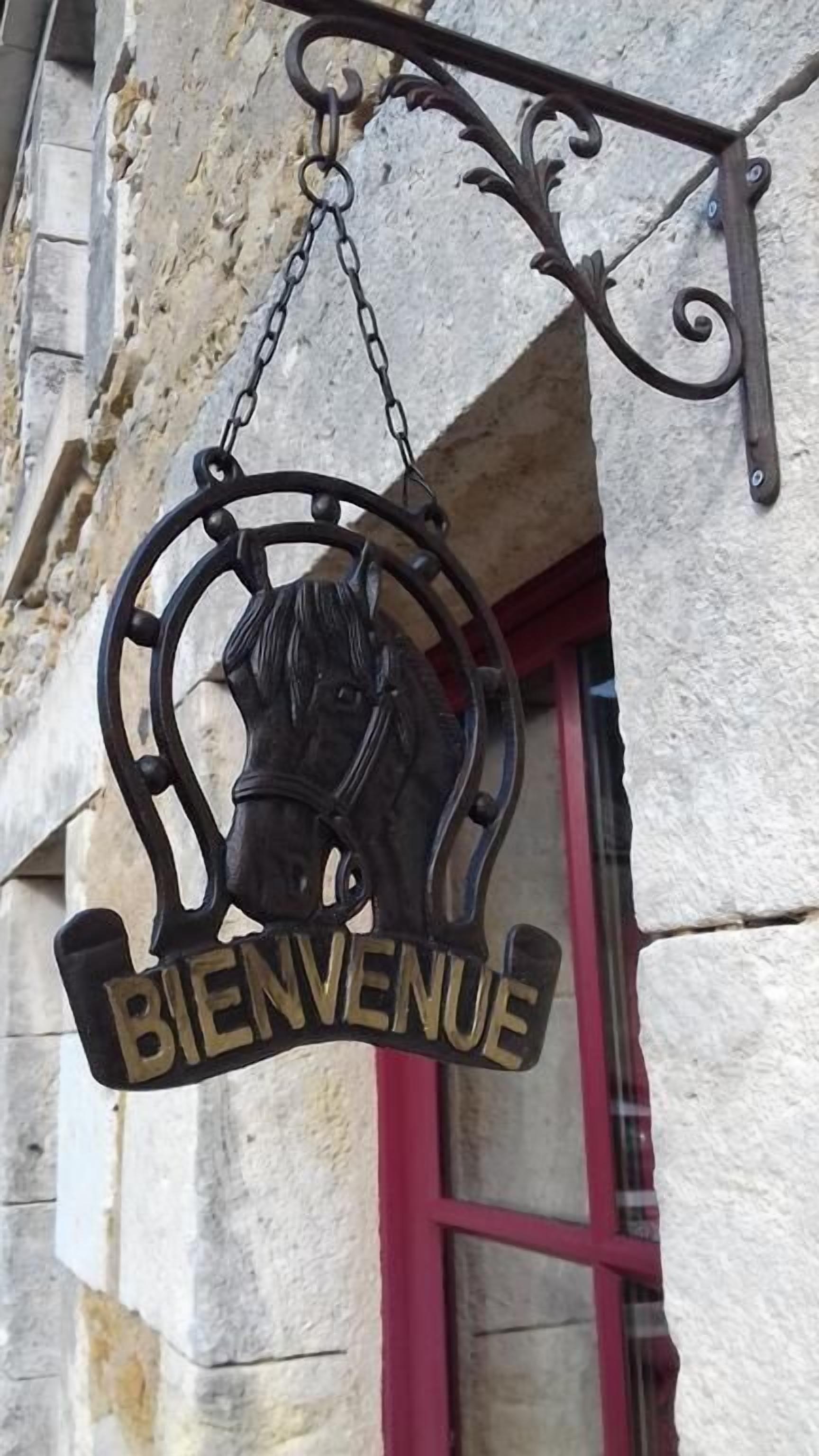 A metal sign with a horse's head and the word "BIENVENUE" hanging from a building.