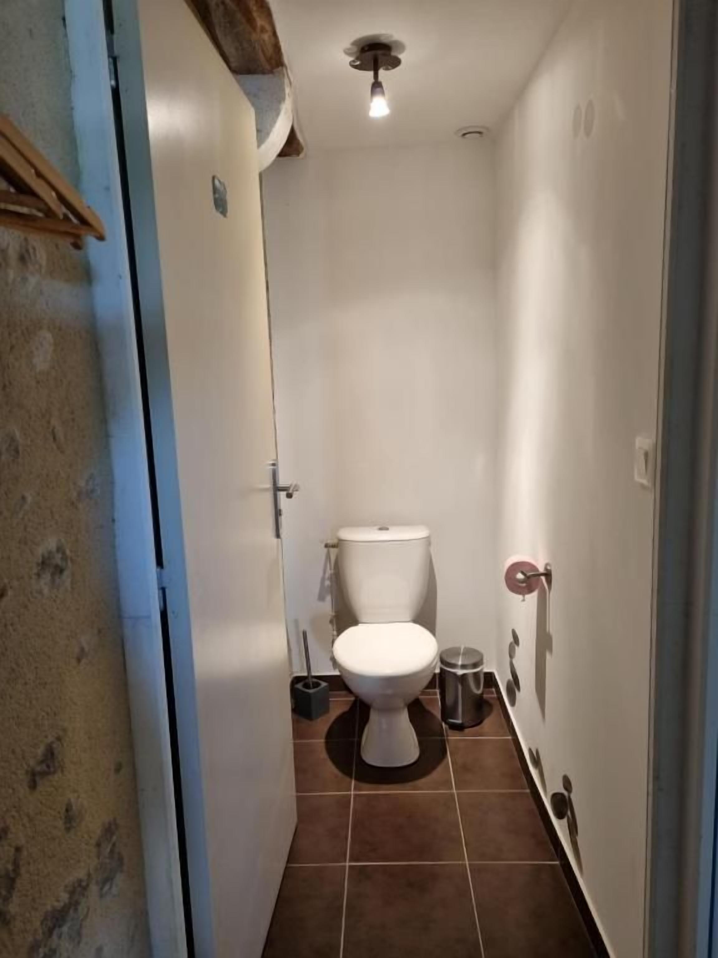 Ein schmales Badezimmer mit Toilette, Mülleimer und einem Handtuchhalter an der Wand.