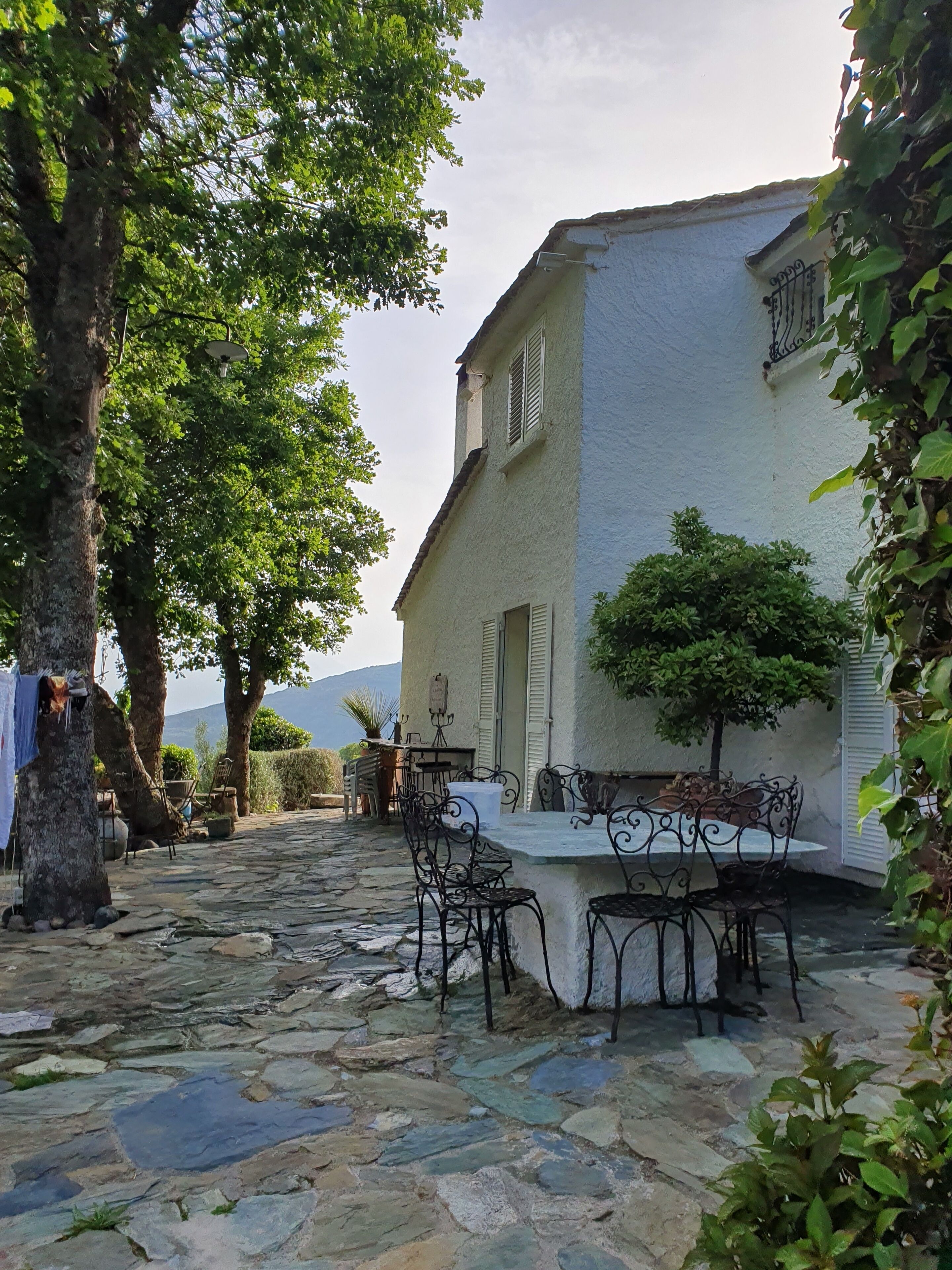 A courtyard with stone flooring, outdoor furniture, and a white building with shutters.