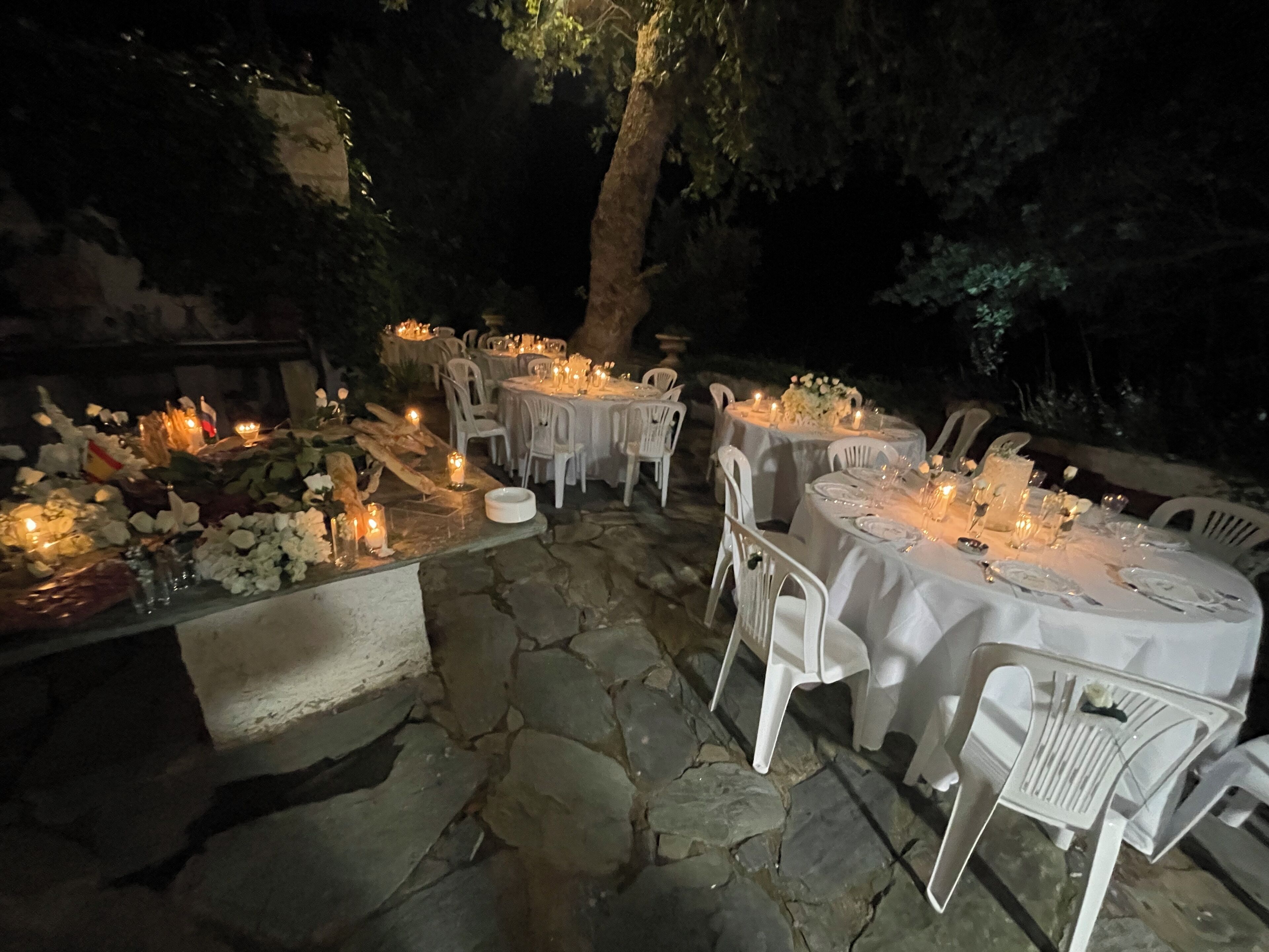 Un espace extérieur aménagé pour les repas, avec un sol en pierre, des chaises en plastique blanches et des tables dressées pour un repas.