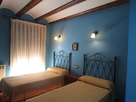 Un dormitorio con dos camas, una ventana con cortinas translúcidas y luces fijadas a la pared.