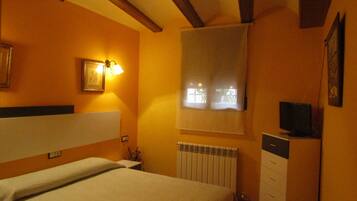 Habitación de hotel con cama, radiador, televisor sobre un mueble y ventana con persianas.
