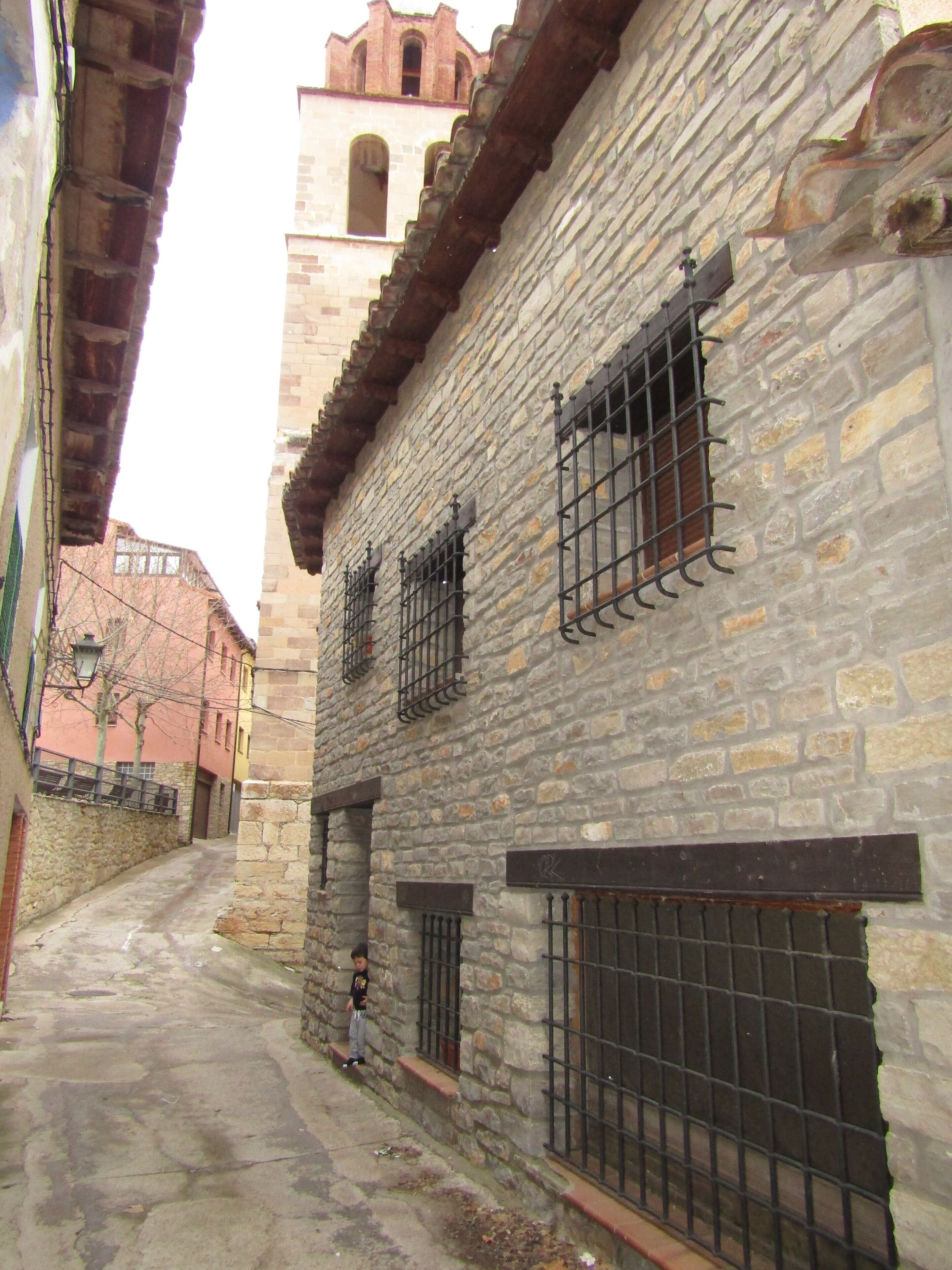 A narrow street with stone buildings, one with barred windows and a visible door.
