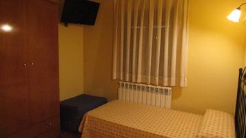 Una habitación con cama, un banco, un armario, un televisor de pantalla plana y una ventana con cortinas.
