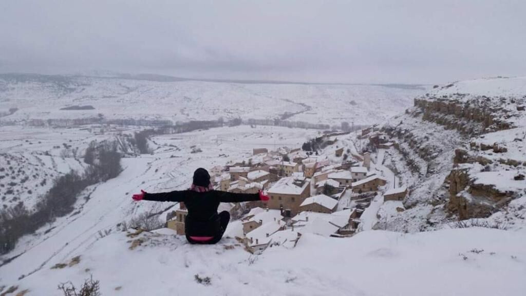 A person sitting on a snow-covered hill overlooking a village with buildings.