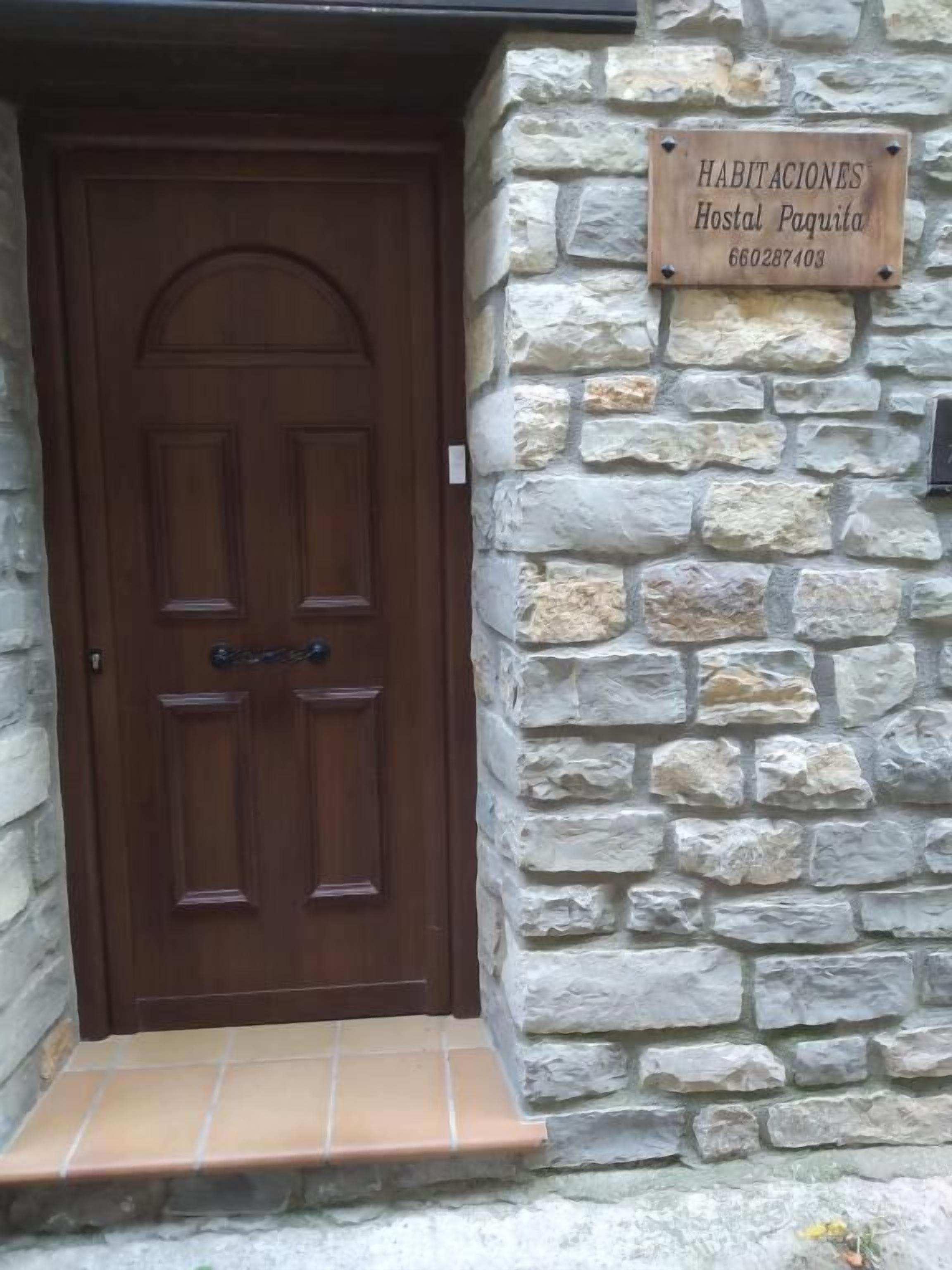 A wooden door with a stone wall and a sign indicating 'Habitaciones Hostal Paquita'.