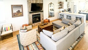 Ein modernes Wohnzimmer mit Kamin, einer Sofagarnitur, einem Couchtisch und einem gemusterten Teppich.