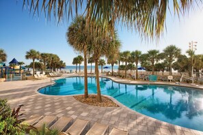 A swimming pool with lounge chairs, palm trees, and a view of the sea. - Life is a BEACH enjoy the WAVES! (Daytona Beach)
