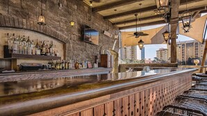 A bar with a stone wall backdrop, wooden bar counter, and hanging lights. - 3BD/Orlando Near Disney - 5 Pools, Game Room, Café and Restaurant On-Site! (Lake Buena Vista)