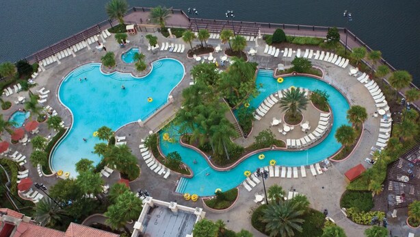 An aerial view of a resort with multiple interconnected swimming pools, surrounded by palm trees and sun loungers. - 3BD/Orlando Near Disney - 5 Pools, Game Room, Café and Restaurant On-Site! (Lake Buena Vista)