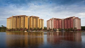 A large hotel complex with multiple high-rise buildings, a body of water in the foreground, and a clear sky. - 3BD/Orlando Near Disney - 5 Pools, Game Room, Café and Restaurant On-Site! (Lake Buena Vista)