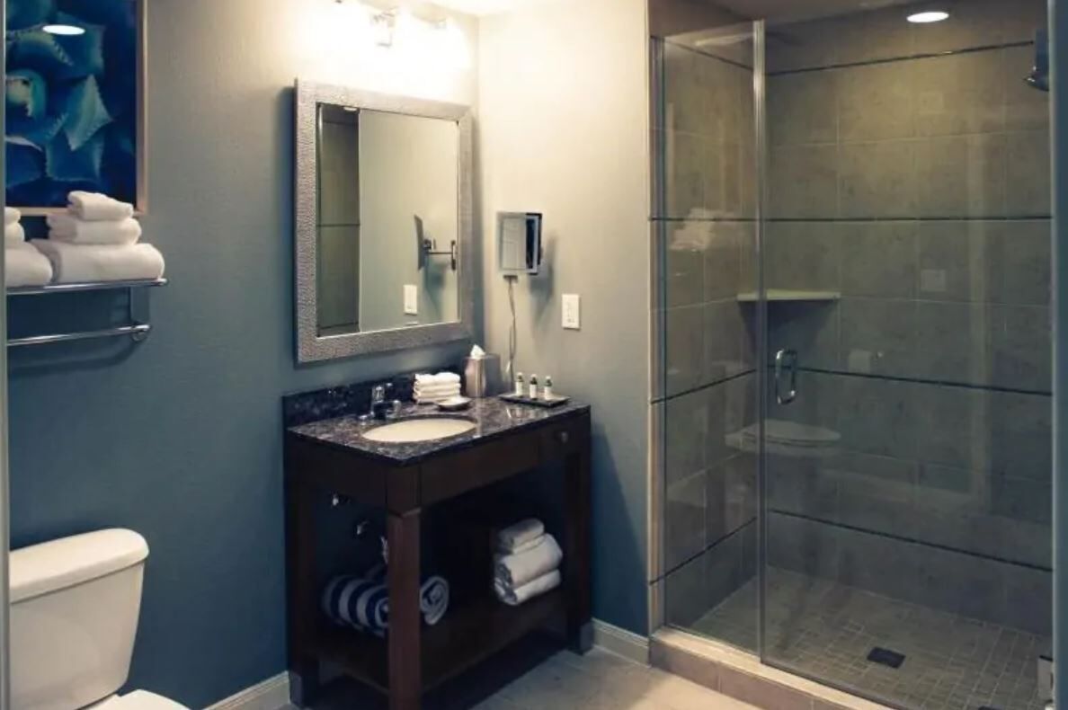 A modern bathroom with a glass-enclosed shower, a sink with a dark countertop, and a mirror above it.