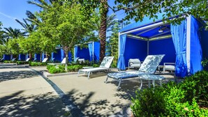 A resort area with outdoor seating under blue canopies, surrounded by greenery and palm trees. - 1BD/Vegas - Pool, Hot Tub, and Shuttle to the Strip! (Las Vegas)