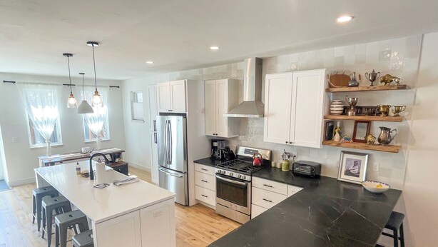 A modern kitchen with white cabinetry, a central island, black marble countertops, stainless steel appliances, and pendant lighting. - Downtown BV Retreat _311_ Steps to Main & River (Buena Vista)