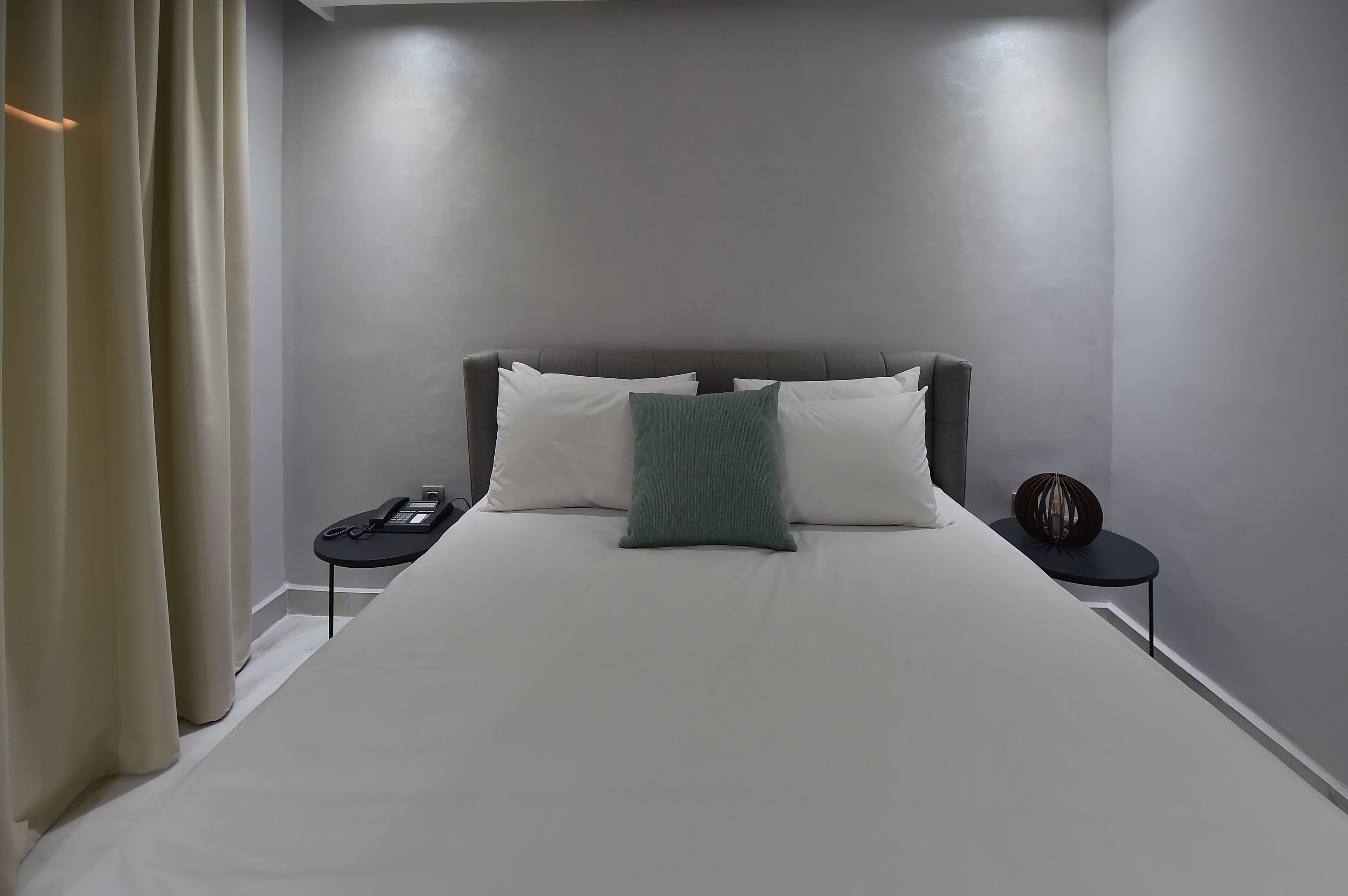 A neatly made bed with white linens and a green pillow, a bedside table with a phone, and a decorative item on the nightstand.