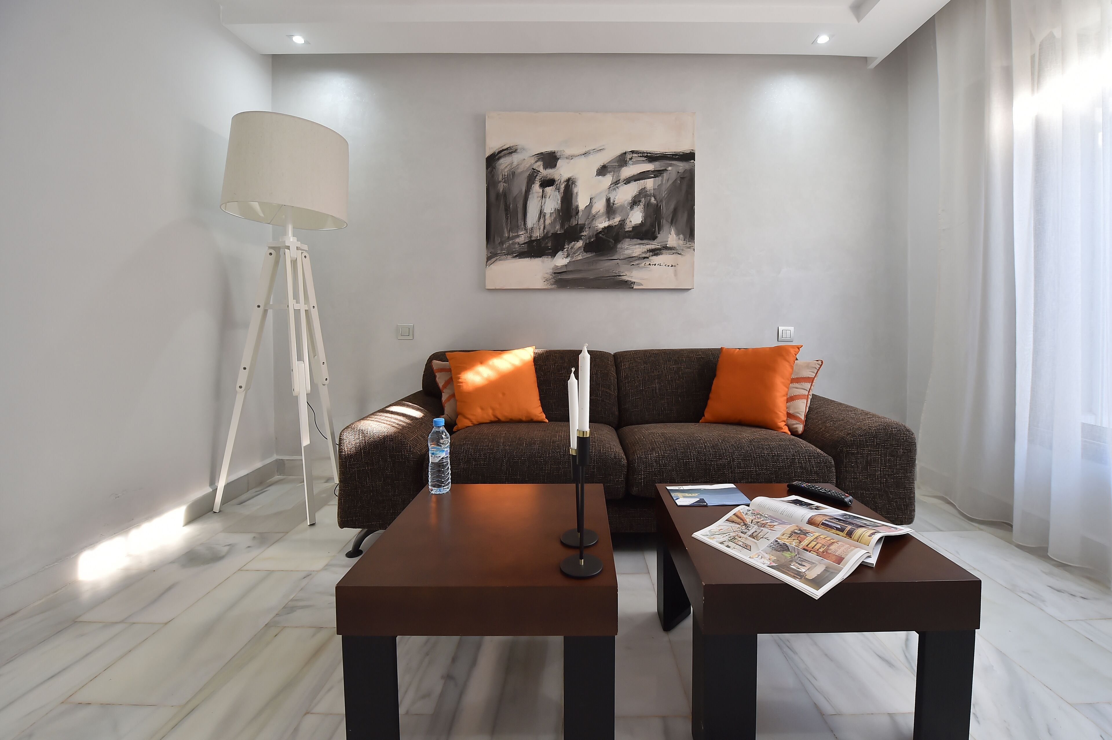 A modern living room with a sofa, two coffee tables, a floor lamp, and a painting on the wall.