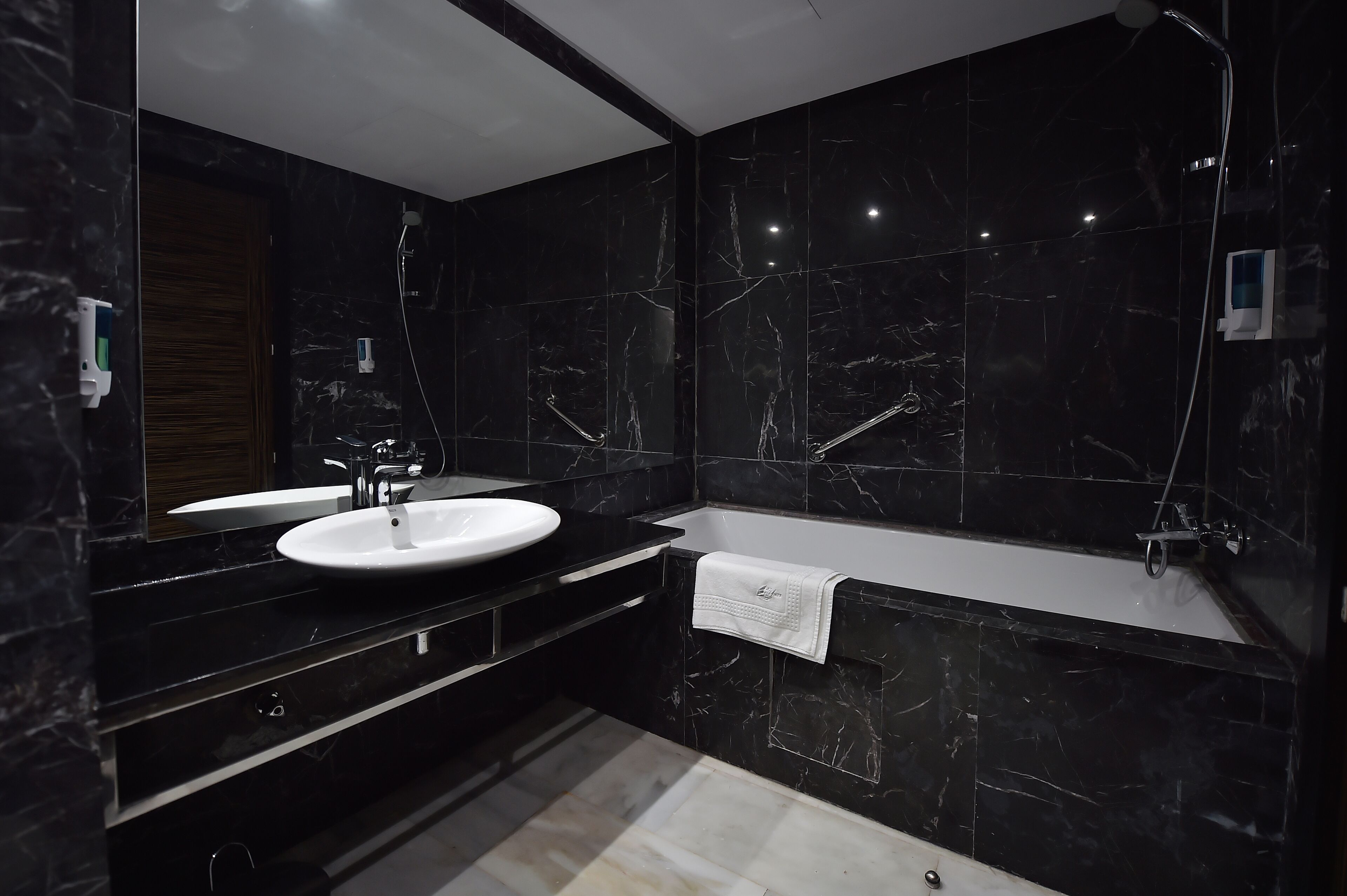 Un baño moderno con lavamanos de mármol negro, bañera blanca y cabezal de ducha de mano.
